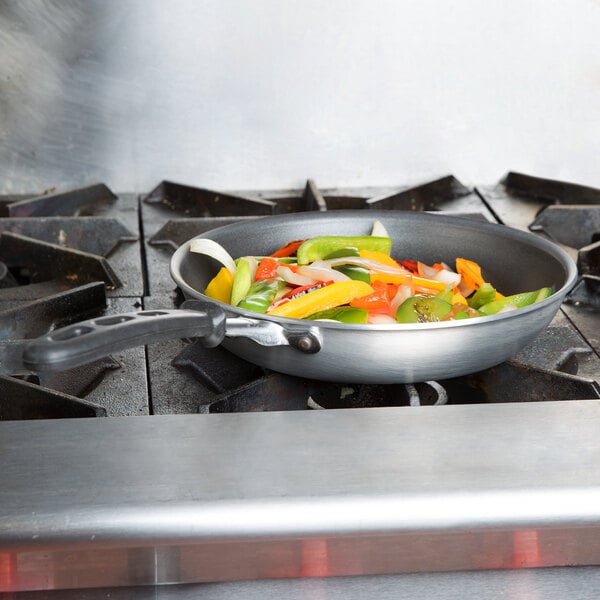 A Vollrath Wear-Ever fry pan with vegetables cooking on a stove.
