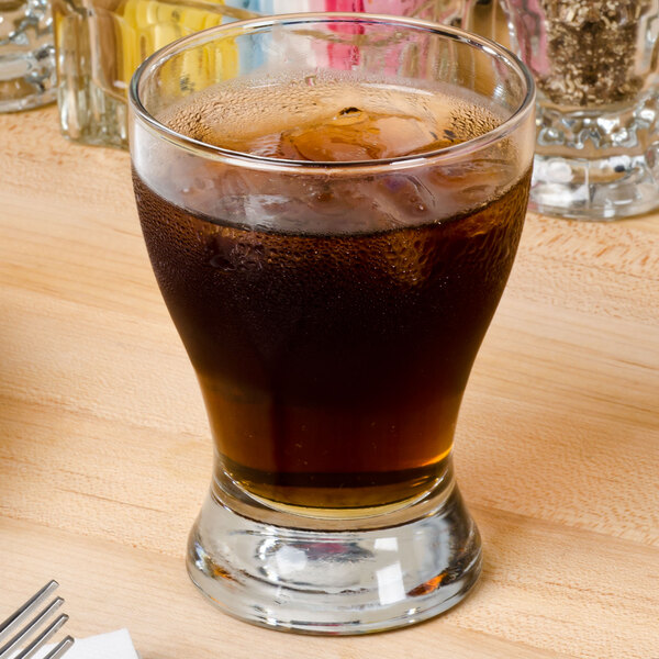 An Anchor Hocking Solace juice glass filled with brown liquid and ice on a table.