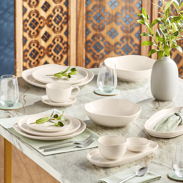 An Acopa Highlands white bowl on a table with plates and bowls.