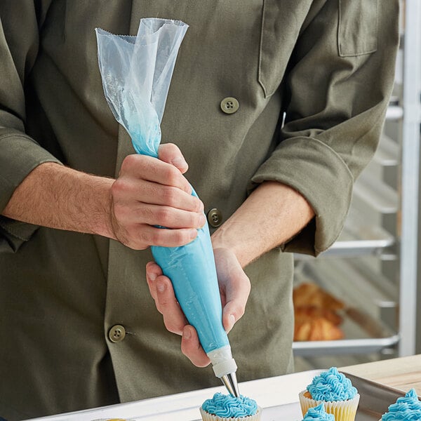 A person's hand holding a pastry bag over a cupcake with blue frosting.