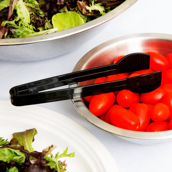 A bowl of salad with a pair of black plastic tongs.