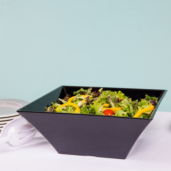 A bowl of salad in a black square melamine bowl on a table.