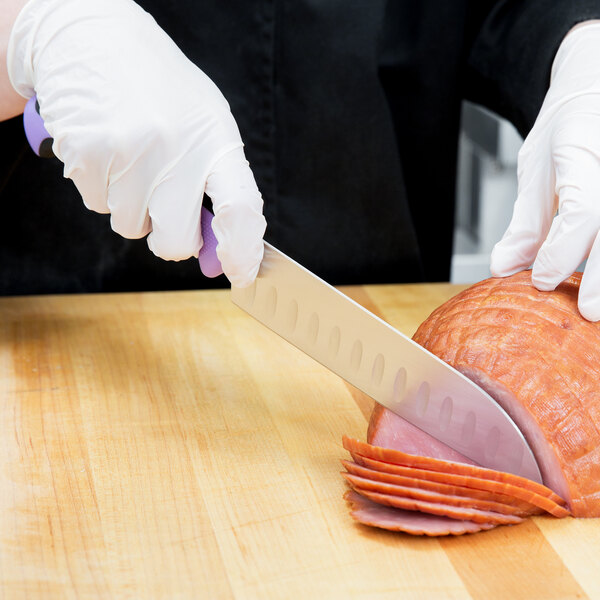 A person wearing white gloves uses a Mercer Culinary Millennia Colors Santoku knife with a purple handle to cut ham.