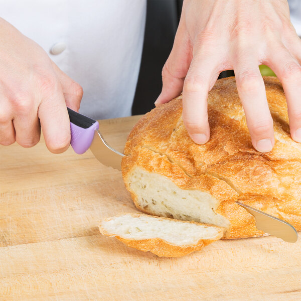 A person using a Mercer Culinary Millennia Colors purple bread knife to cut a loaf of bread.