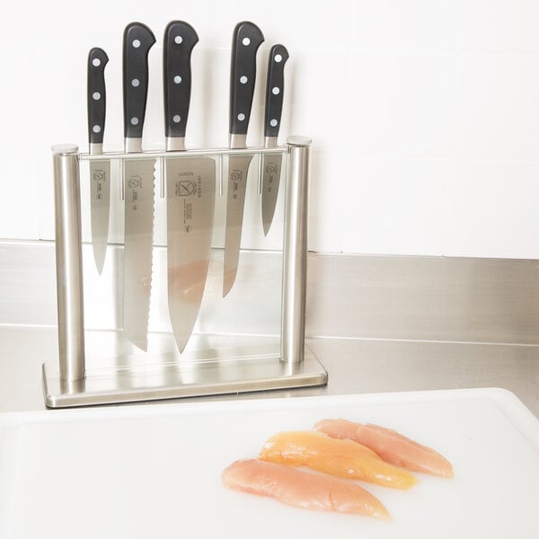 A Mercer Culinary Renaissance knife set in a knife block on a counter next to raw chicken.