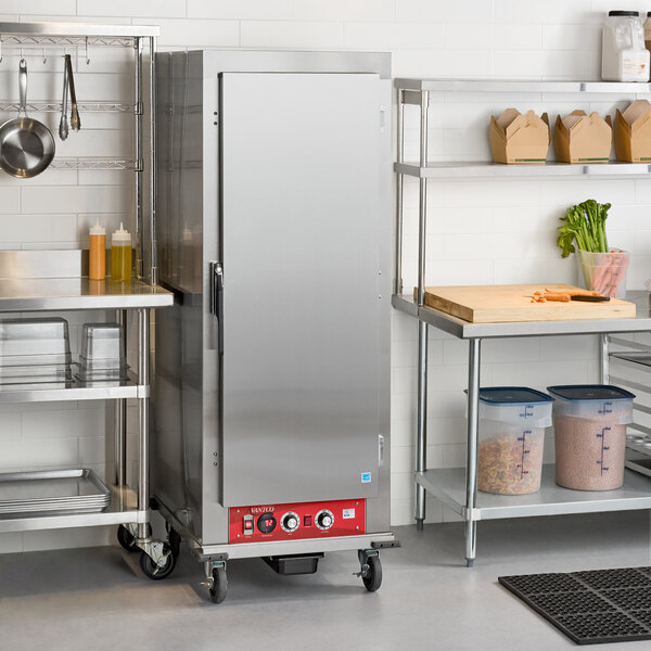 A tall, stainless steel cabinet with a solid door and control panel at the bottom, situated on wheels in a commercial kitchen setting.