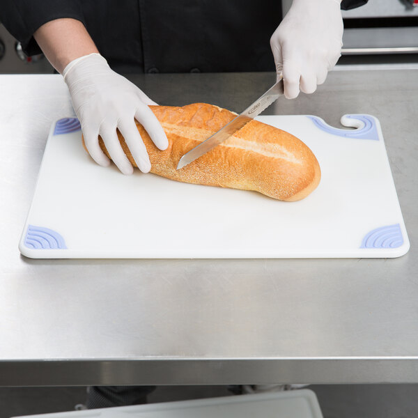 A person cutting a loaf of bread on a San Jamar white cutting board.