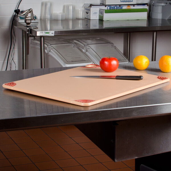 A San Jamar brown cutting board on a counter with a knife and fruit.