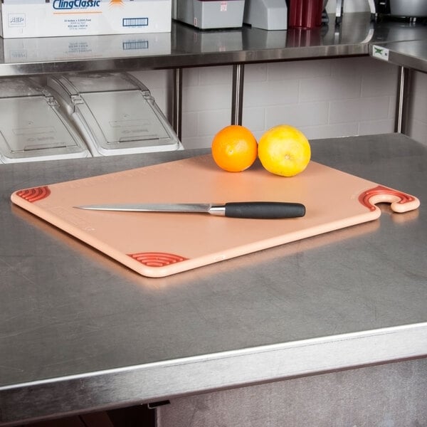 A San Jamar brown cutting board with a knife and oranges on a counter.