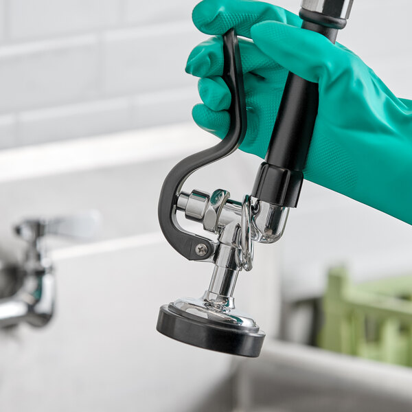 A chrome spray nozzle with a black handle and rubber tip, shown being held by a gloved hand.