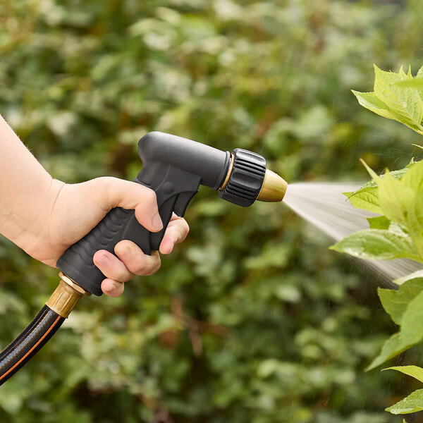 A hand using a Regency black plastic double trigger spray nozzle to water a plant with a garden hose.