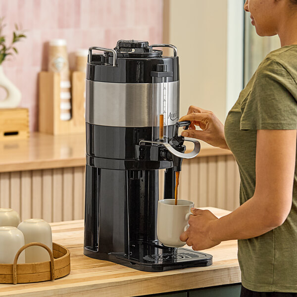 A woman pouring coffee into an Avantco thermal coffee server on a counter.