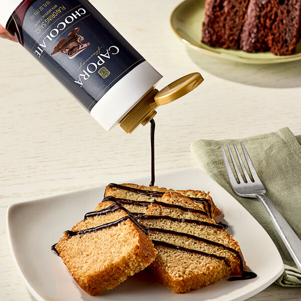 A plate of cake with Capora chocolate flavoring sauce being poured over it.