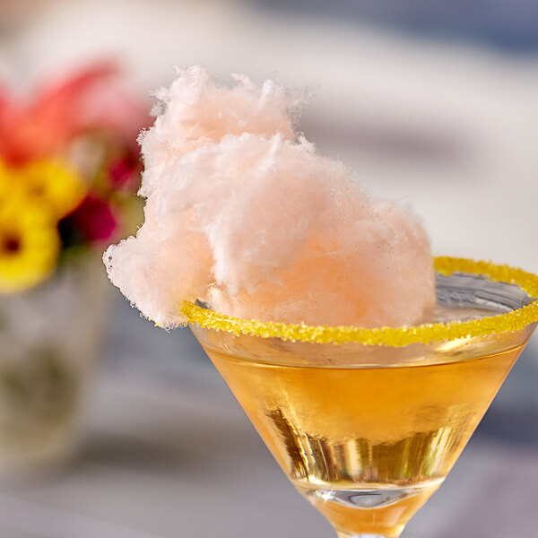A glass of yellow liquid with Great Western orange cotton candy on the rim.