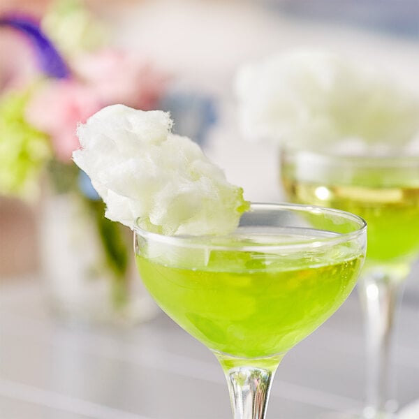 A pair of glasses with a green liquid and cotton candy on the rim.