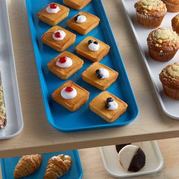 A blue Cambro market tray of pastries and desserts on a counter.