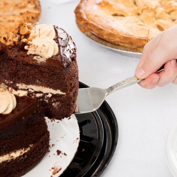 A person using an American Metalcraft stainless steel pastry server to cut a chocolate cake.