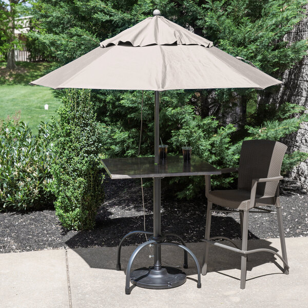 A table with two chairs and a Grosfillex Windmaster umbrella on a patio.
