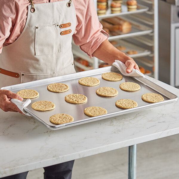 A person holding a Baker's Lane USA aluminum bun pan filled with cookies.