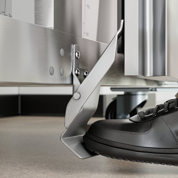 A right foot pedal kit attached to the base of a stainless steel unit, shown being operated by a person wearing a black shoe.