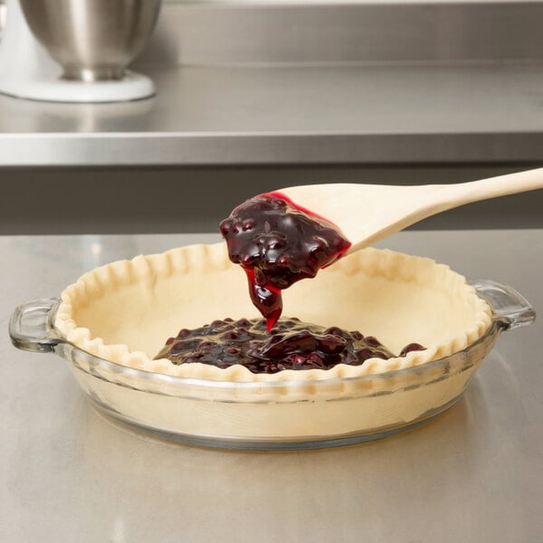 A wooden spoon pouring red liquid into a glass pie pan.