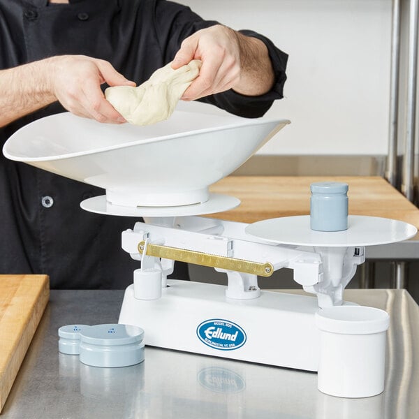 A man using an Edlund baker's dough scale to weigh dough on a counter.