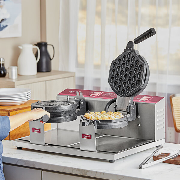 A person using an Estella double waffle maker to make bubble waffles.