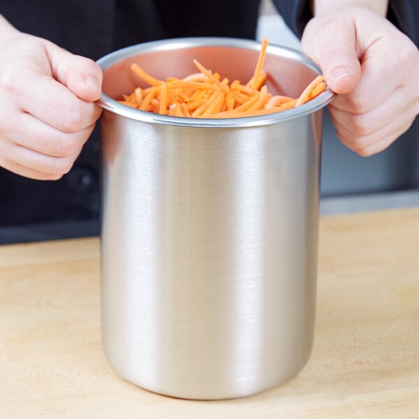 A person holding a Vollrath stainless steel container full of carrots.