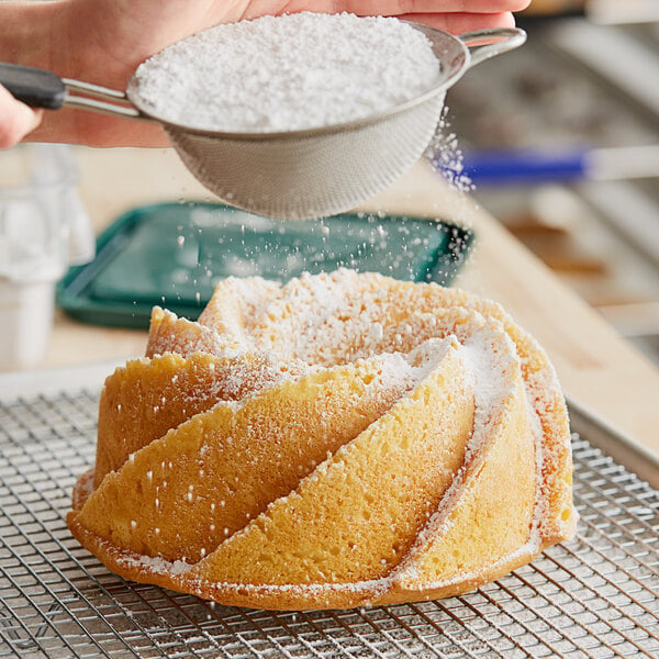 A person pouring Domino 10X Confectioners Sugar on a cake.