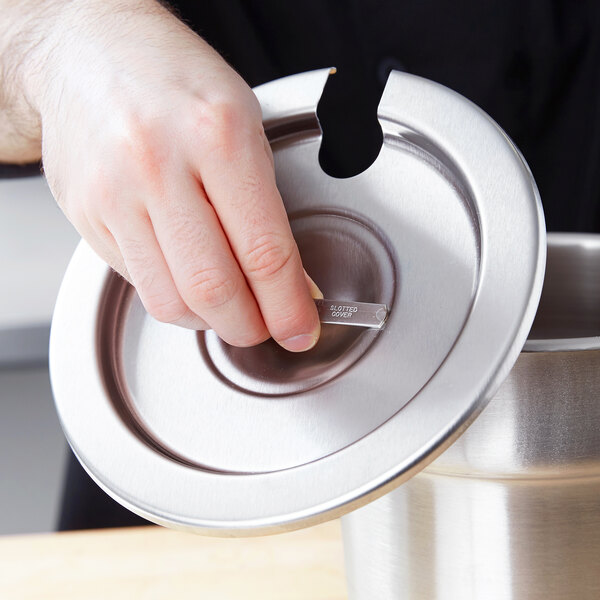 A hand using a Vollrath stainless steel slotted cover on a metal container.