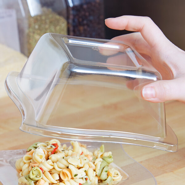 A hand holding a Fineline clear dome lid over pasta in a clear container.