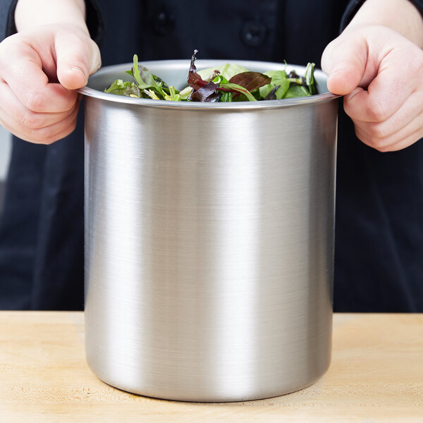 A person holding a Vollrath stainless steel bain marie pot filled with salad.