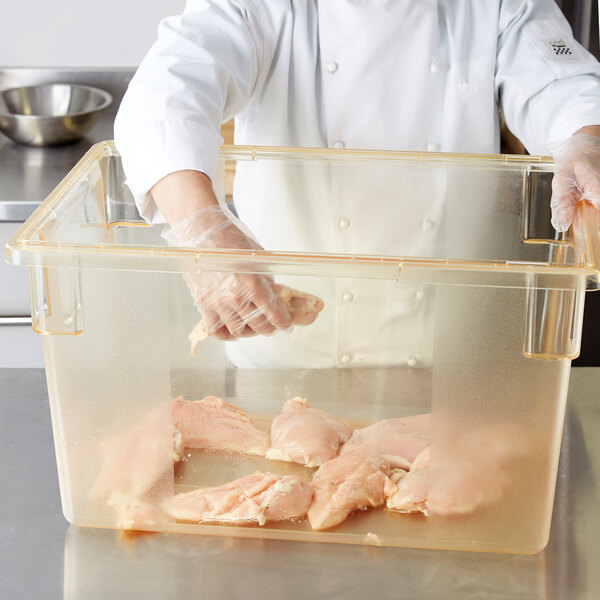 A person holding a Carlisle yellow plastic food storage container filled with raw chicken.