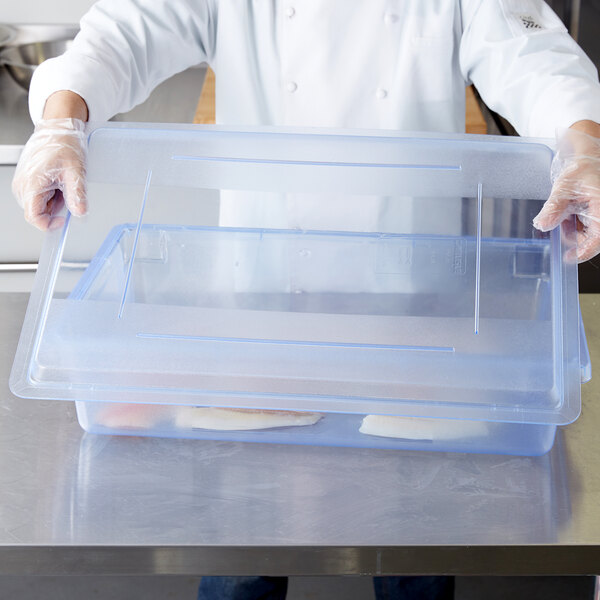 A chef holding a Carlisle clear plastic container with blue lid full of food.