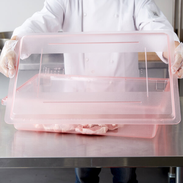 A person holding a Carlisle red lid on a plastic container filled with meat.