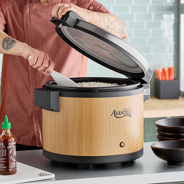 A man using an Avantco woodgrain electric rice warmer to cook rice on a counter.