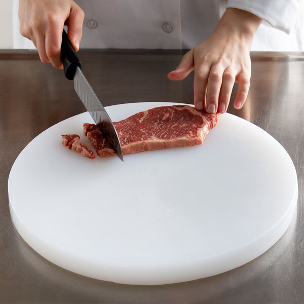 A person cutting a piece of meat on a white polyethylene cutting board.