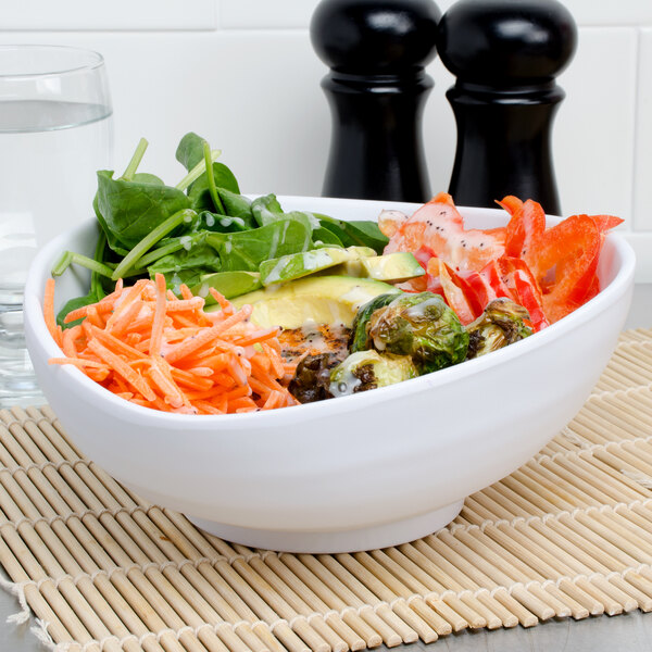 A white Elite Global Solutions oval bowl filled with vegetables and greens.