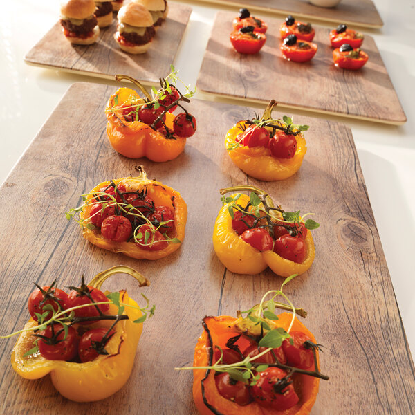 A rectangular melamine serving board with tomatoes, herbs, and a yellow bell pepper on a table.