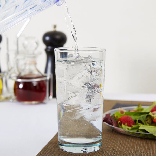 A close up of a glass of water with a lemon slice on a table with a plate of salad.