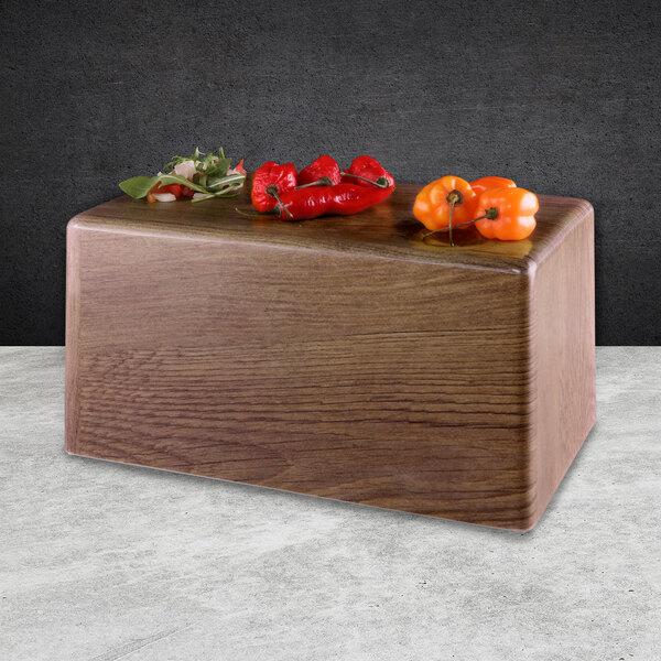 A rectangular wooden faux walnut riser with peppers on a wood surface.