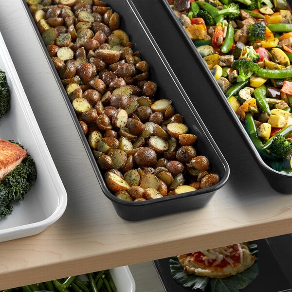 A black fiberglass market pan on a counter filled with a variety of green vegetables.