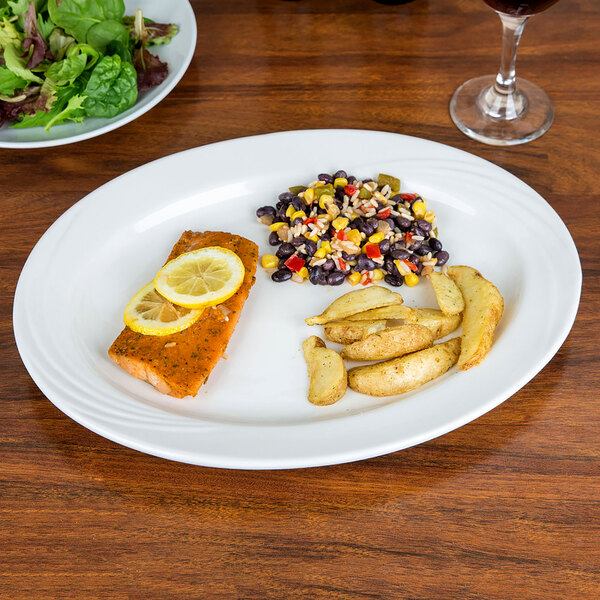 A CAC porcelain platter with a plate of green and red salad and a piece of food with lemon slices on top on a table.