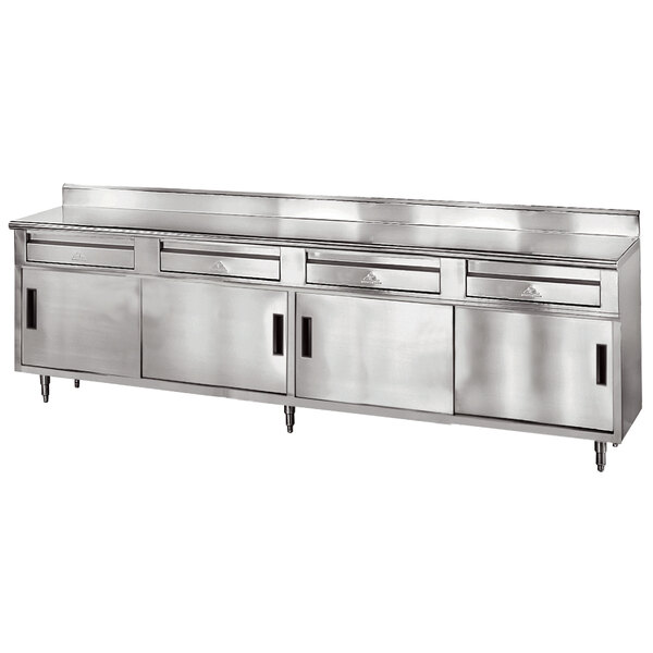 A stainless steel Advance Tabco enclosed base work table with 4 drawers and 4 sliding doors.