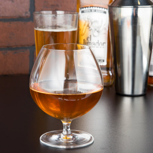 A Stolzle brandy snifter filled with brown liquid on a table in a cocktail bar.