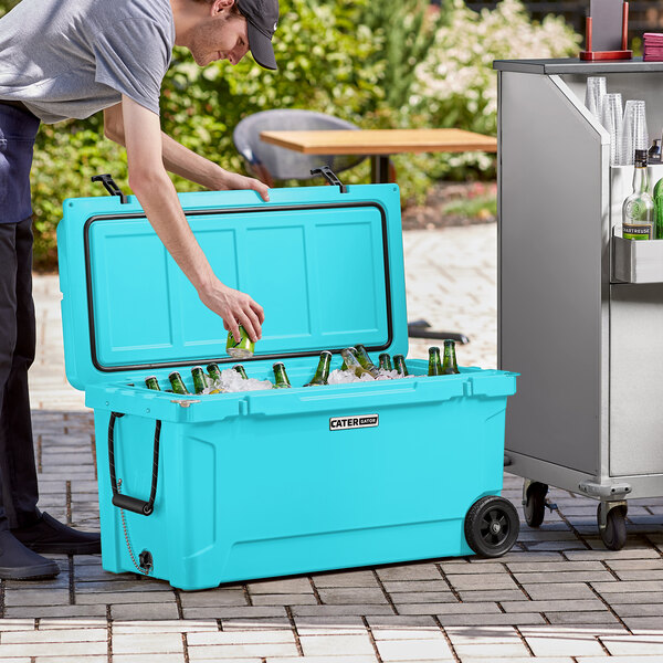 A man opening a CaterGator sky blue cooler to put beer and a green bottle inside.