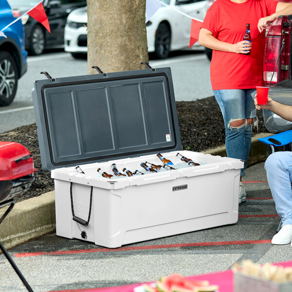 A man sitting in a blue chair next to a CaterGator outdoor cooler filled with beer bottles.