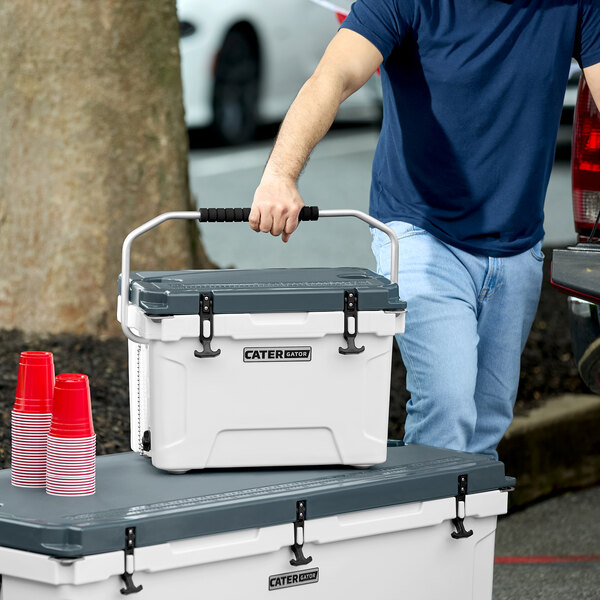 A person in a blue shirt carrying a white CaterGator outdoor cooler.