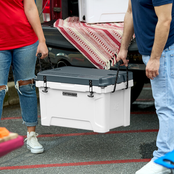 A man and woman carrying a white CaterGator outdoor cooler with a black stripe on the lid.