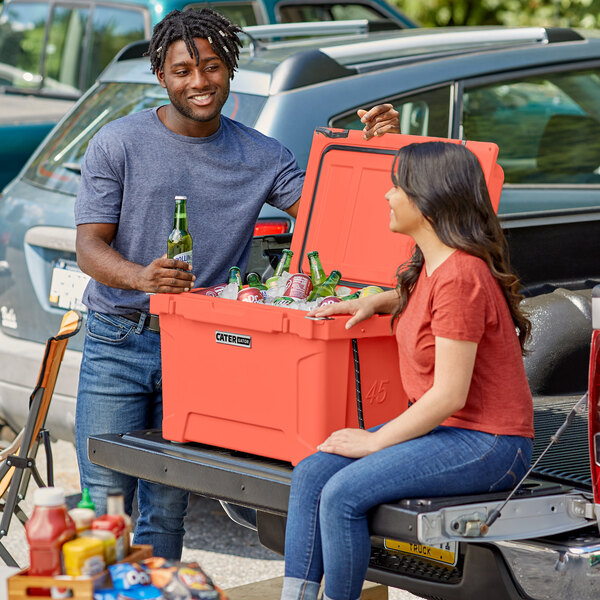 A man and woman sitting on the back of a truck with a CaterGator cooler.
